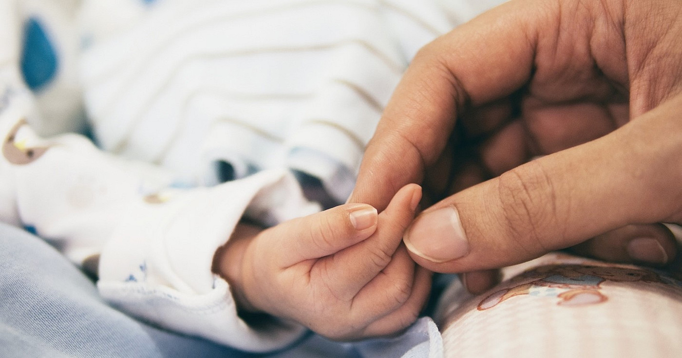 A close-up photograph of a woman holding an infant’s hand.