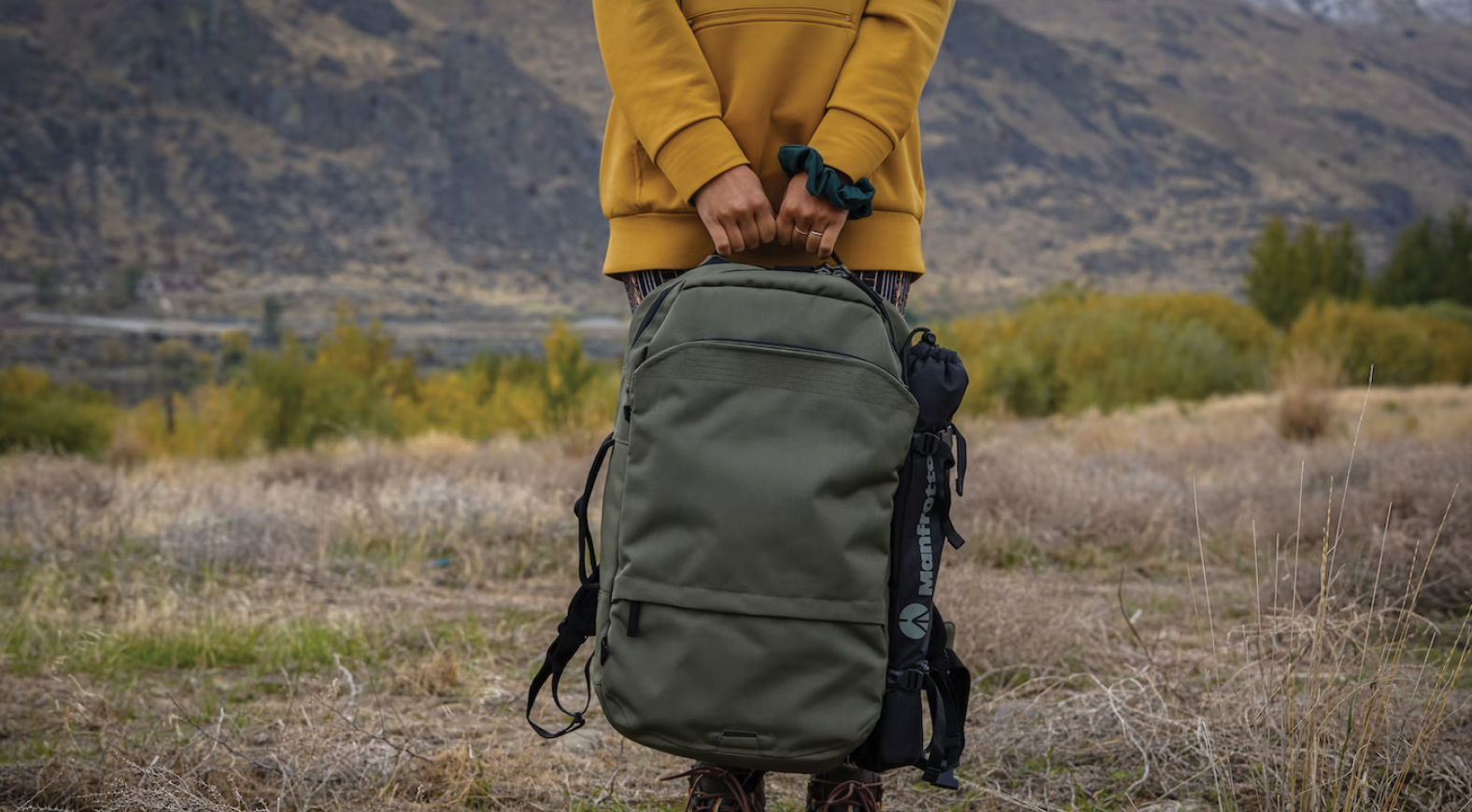 anonymous person stands alone in a field holding a large backpack